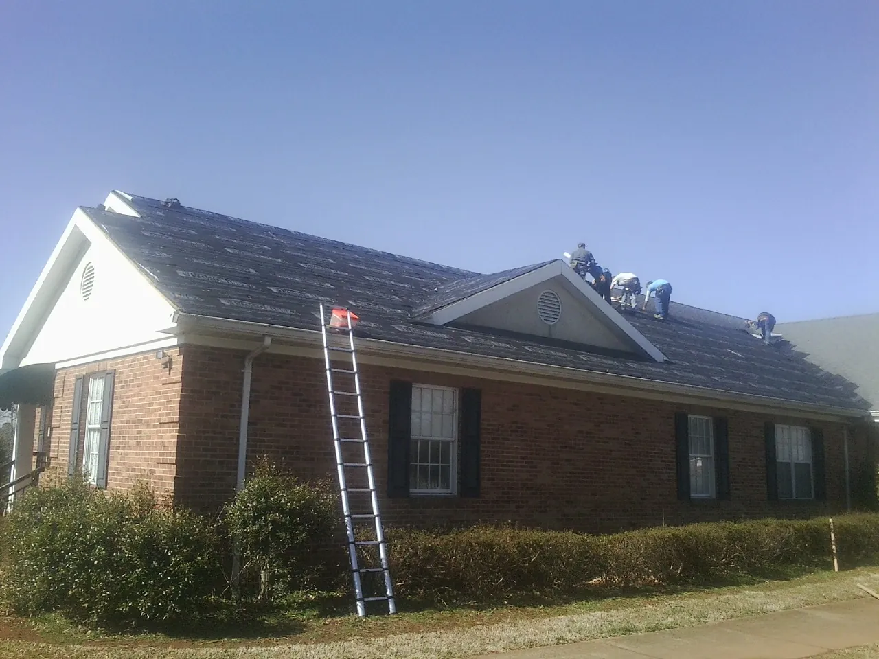 Crew tearing shingles off a brick ranch roof with a ladder set — Metal Roof Repair work by our crew in Mindoro