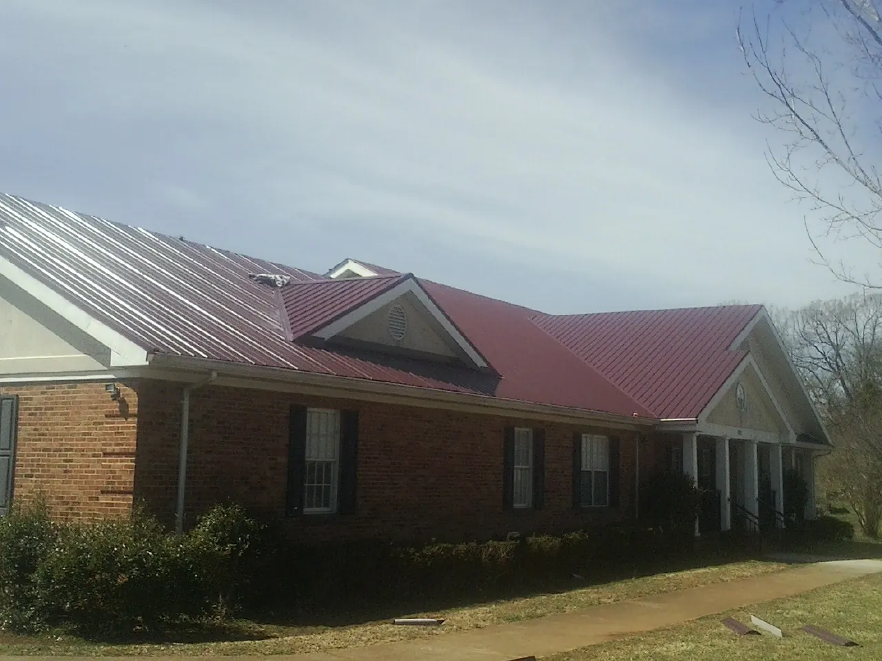 Red metal roof with gabled entries on a long brick building, from a Hail Damage Roof Repair job in Mindoro