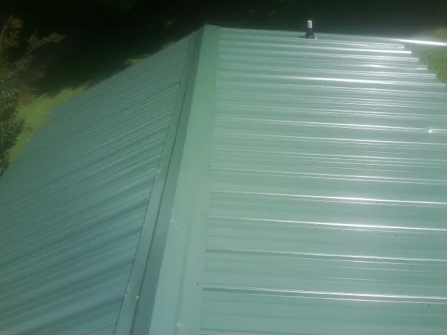 New green metal panels meeting at the ridge of a roof — Flat Roof Repair work by our crew in Mindoro
